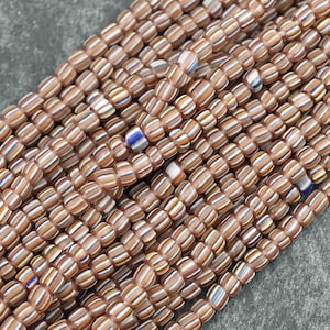 May include: A strand of brown, white, and blue striped glass beads. The beads are small and cylindrical, and they are arranged in a random pattern.