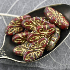 May include: A group of red and gold glass beads with a decorative pattern. The beads are shaped like a teardrop and have a speckled finish.
