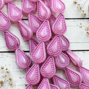 Op de afbeelding: Een verzameling traanvormige kralen in een levendige roze tint. Elke kraal heeft een glad, verhoogd midden omringd door een textuurrand van kleine, uniforme stippen. De kralen hebben een glanzende afwerking en zijn in een losse groep gerangschikt.