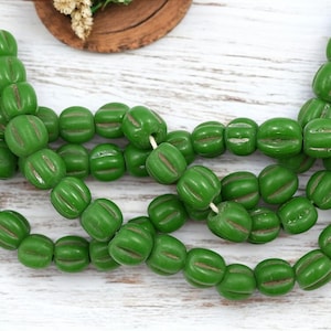 May include: Strands of green, melon-shaped beads with carved lines. The beads are strung together, creating a necklace or bracelet. The beads are a vibrant green color, and the lines are a lighter shade of green.