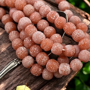 May include: A strand of brown glass beads with a white speckled finish. The beads are round and have a frosted appearance.