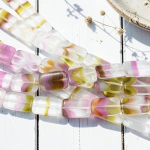 May include: Strands of rectangular glass beads in shades of pink, yellow, and brown. The beads have a translucent quality, with the colors swirled within. The beads are strung together, suggesting they are for jewelry making or crafting.