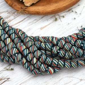 May include: Strands of dark teal beads with colorful stripes of red, white, and yellow. The beads are arranged in a curved pattern, showcasing their design. The beads are likely for jewelry making or crafting.