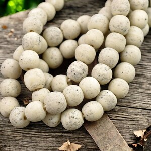 May include: A strand of off-white beads with a speckled texture. The beads are round and have a natural, organic look.