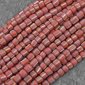 May include: A strand of pink, white, and orange glass beads. The beads are square shaped and have a striped pattern.
