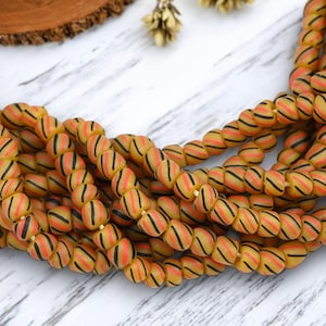 May include: Strands of yellow glass beads with orange and black stripes. The beads are oval-shaped and strung together, creating a textured and colorful accessory. The beads are a warm, earthy tone, perfect for jewelry making.