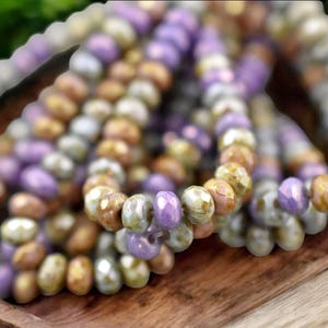 May include: A strand of glass beads in shades of purple, brown, and white. The beads are faceted and have a slightly iridescent finish.