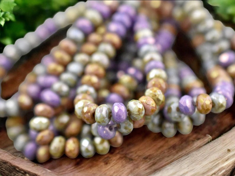 May include: A strand of glass beads in shades of purple, brown, and white. The beads are faceted and have a slightly iridescent finish.