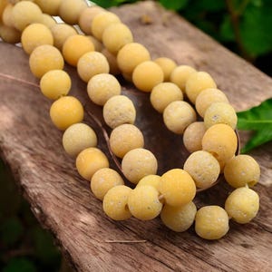 May include: A strand of yellow agate beads with a textured surface. The beads are round and have a matte finish.