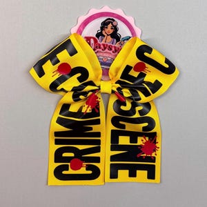 May include: Yellow and black ribbon bow with the words "Crime Scene" and red blood splatter.