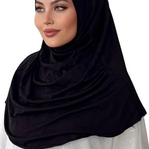 May include: A black jersey hijab with a smooth, silky texture. The hijab is draped around the head and neck, creating a simple and elegant look.