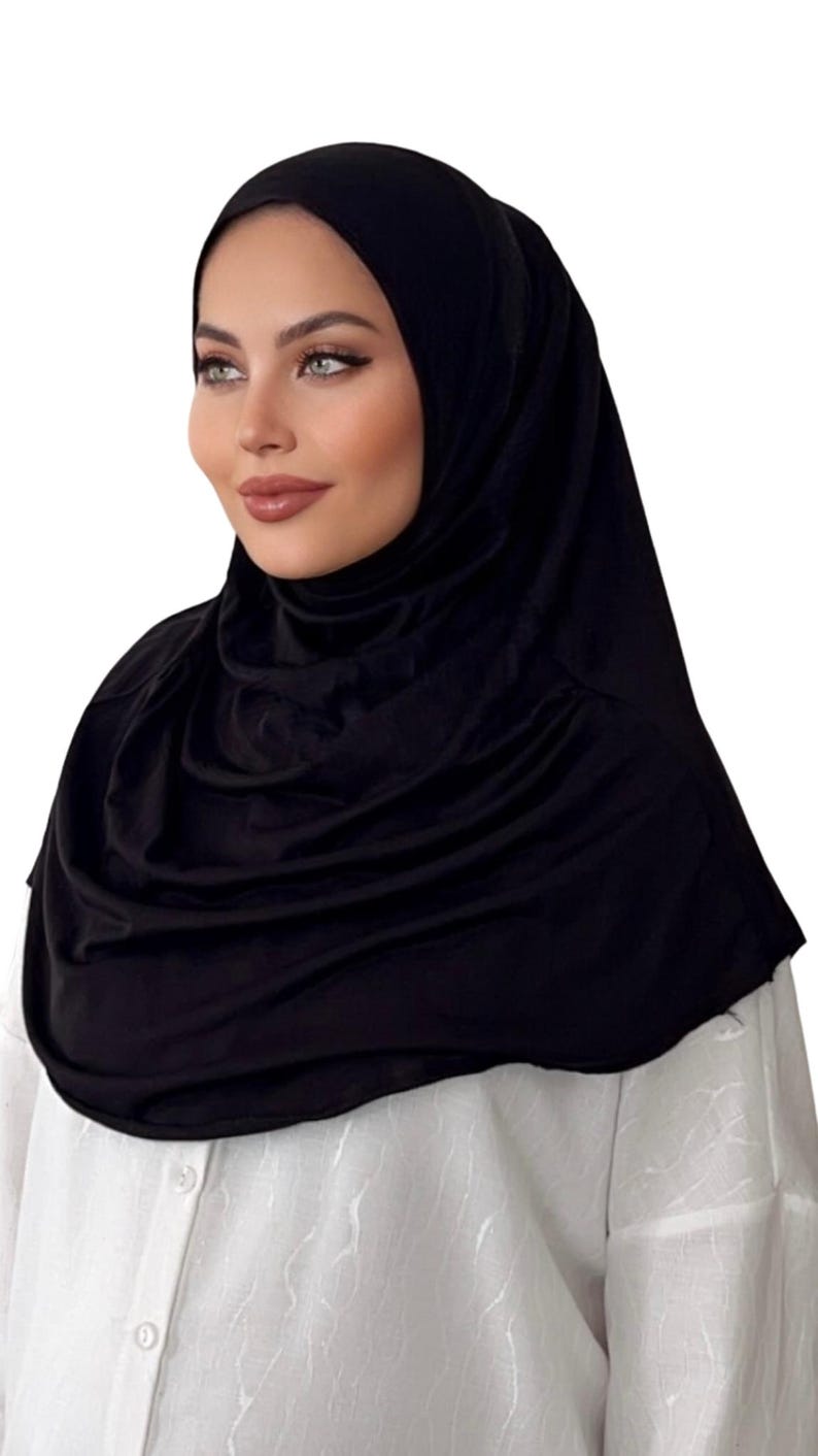 May include: A black jersey hijab with a smooth, silky texture. The hijab is draped around the head and neck, creating a simple and elegant look.