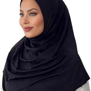 May include: A black jersey hijab with a smooth, stretchy fabric. The hijab is draped over the head and neck, creating a simple and elegant look.