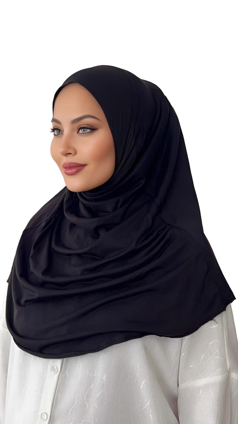 May include: A black jersey hijab with a smooth, stretchy fabric. The hijab is draped over the head and neck, creating a simple and elegant look.