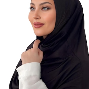 May include: A black jersey hijab with a smooth, silky texture. The hijab is worn by a person with a white shirt.