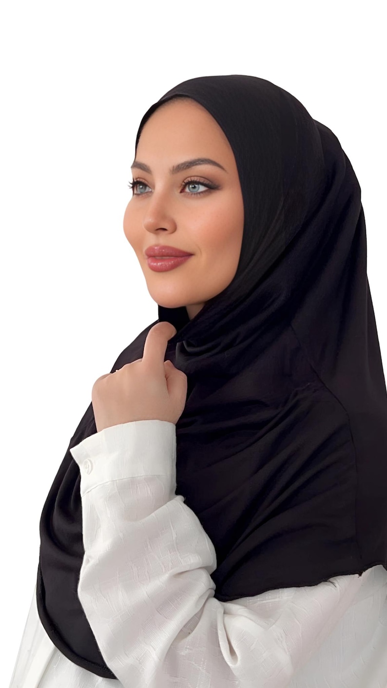 May include: A black jersey hijab with a smooth, silky texture. The hijab is worn by a person with a white shirt.