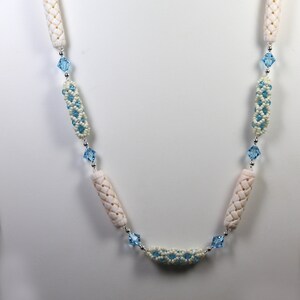 May include: A long necklace with white and blue beads. The necklace features white cylindrical beads with a woven pattern and blue crystal beads.