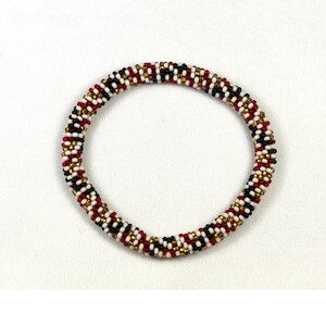 May include: A beaded bracelet with a spiral design. The bracelet features a pattern of red, white, black, and gold beads. The bracelet is a circular shape and is likely worn on the wrist.