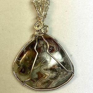 May include: A silver wire wrapped pendant featuring a brown, white, and gray agate stone with a swirling pattern.