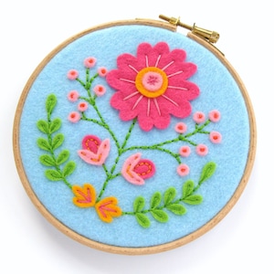 May include: A blue felt hoop with a pink flower, green leaves, and orange flowers embroidered on it.