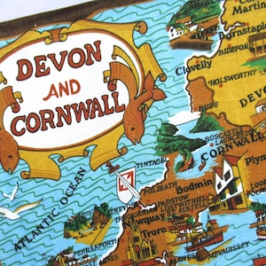 May include: A vintage map of Devon and Cornwall, featuring a detailed illustration of the region. The map includes the text "DEVON AND CORNWALL" in a decorative frame, with the Atlantic Ocean and various towns labeled.