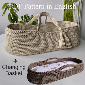 Op de afbeelding: Een gehaakte baby-wikkelmand met een handvat en een bijpassende verschoningsmat. De mand is beige en de mat is bruin. De tekst "PDF Pattern in English + Changing Basket" is zichtbaar in de afbeelding.