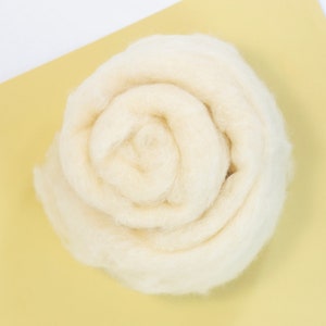 May include: A close-up of a white, fluffy ball of wool yarn, rolled into a spiral shape, on a yellow background.