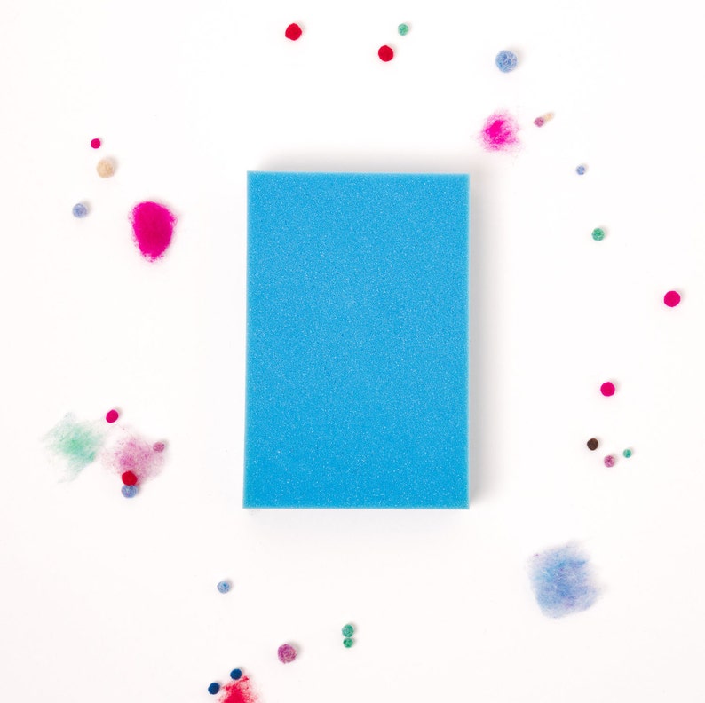 Pu&ograve; includere: Una spugna rettangolare blu su uno sfondo bianco circondata da piccole palline di feltro colorate.