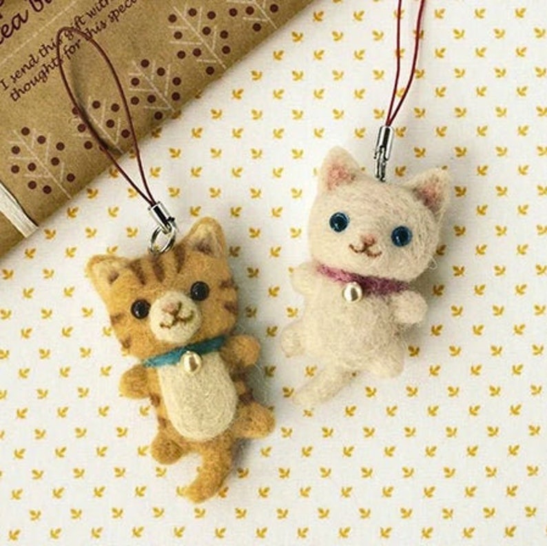 Pu&ograve; includere: Due portachiavi in feltro a forma di gatto, uno tigrato arancione e bianco e l'altro bianco, con un cordino marrone attaccato a ciascuno. I gatti indossano piccole campane d'argento intorno al collo.