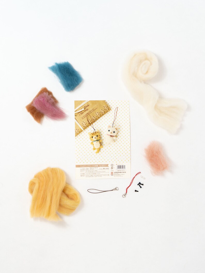 Pu&ograve; includere: Un kit di feltro con lana di vari colori, tra cui giallo, rosa, blu e bianco. Il kit include anche uno spago rosso, due perline nere e un piccolo cartoncino con le istruzioni. Il cartoncino ha il testo "Happy You" e una piccola illustrazione di due gatti.