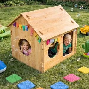 May include: A wooden playhouse with two round windows, decorated with colorful flags, sits on a grassy lawn. Two children are visible inside the playhouse. Other toys include a yellow truck, a blue whale, and a green picnic table.