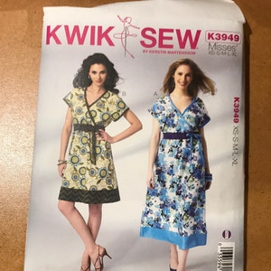 May include: Sewing pattern envelope for a wrap dress with short sleeves. The pattern is for misses sizes XS-S-M-L-XL. The envelope shows two models wearing the dress in different floral prints. The pattern is by Kwik Sew and designed by Kerstin Martensson.