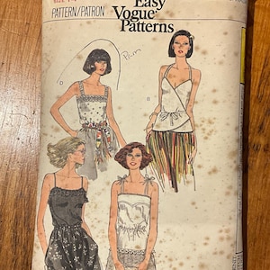 May include: Vintage Vogue Patterns sewing pattern, size 14. The cover features illustrations of four different women's outfits, including dresses and tops. The pattern is for tops and is stretchable. The cover is aged with visible wear and tear.