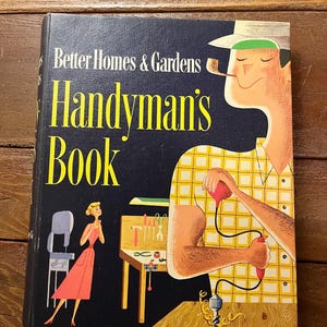 May include: A vintage book titled "Handyman's Book" by Better Homes & Gardens. The cover features a cartoon illustration of a man in a yellow plaid shirt using a drill and a woman in a pink dress looking on.