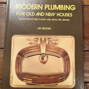 May include: A book titled "Modern Plumbing for Old and New Houses" by Jay Hedden. The book cover features a close-up of a shiny, copper-colored bathroom sink.