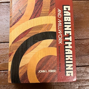 May include: A red book titled "Cabinetmaking and Millwork, Second Edition, Revised" by John L. Feier. The cover features a colorful abstract design of wood grain.