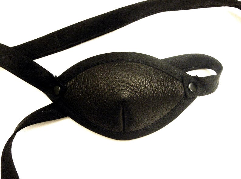 Pu&ograve; includere: Fascetta per occhi in pelle nera con superficie strutturata e cinturino in tessuto nero. La fascetta per occhi &egrave; di forma ovale e ha un bordo cucito. Il cinturino &egrave; regolabile e fissato con un bottone.