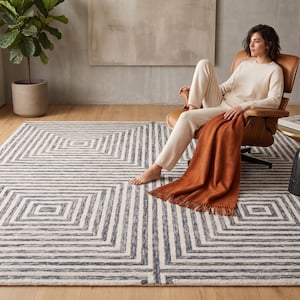 May include: A large rectangular area rug featuring a repeating geometric pattern of concentric squares in dark charcoal gray and off-white. The rug has a low-pile texture and covers a significant portion of the light-colored wooden floor space.