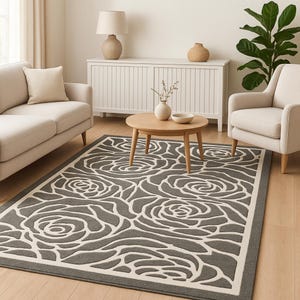 Op de afbeelding: Een grijs en wit vloerkleed met een bloemenrozenpatroon. Het vloerkleed heeft grote, gestileerde rozenontwerpen in wit tegen een grijze achtergrond. Het vloerkleed is rechthoekig en heeft een witte rand.