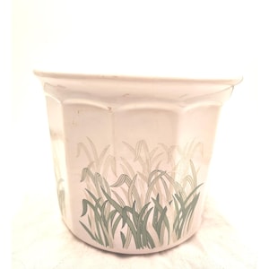 Op de afbeelding: Een witte keramische plantenbak met een geometrische vorm en een groen grasontwerp. De plantenbak heeft een licht uitlopende rand en een getextureerd oppervlak. Het grasontwerp is een herhalend patroon.
