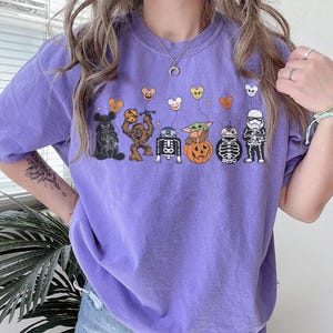 Puede incluir: Una camiseta morada con un dise&ntilde;o de Halloween de Star Wars. El dise&ntilde;o incluye a Darth Vader, Chewbacca, R2-D2, Baby Yoda, un droide esqueleto y un Stormtrooper, cada uno con un toque de Halloween.