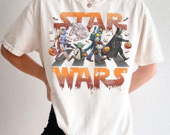 Puede incluir: Camiseta color crema con un diseño de Star Wars con temática de Halloween. El gráfico muestra personajes como Darth Vader y Yoda cruzando una calle, sosteniendo calabazas. Las palabras "STAR WARS" están en naranja, con un efecto de telaraña.