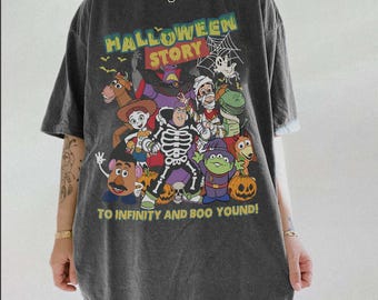 Puede incluir: Una camiseta gris carbón de manga corta con un estampado gráfico que incluye el texto HALLOWEEN STORY y TO INFINITY AND BOO YOUND. El diseño muestra personajes de dibujos animados disfrazados, calabazas, una telaraña y murciélagos.