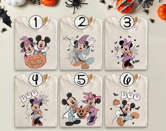 Puede incluir: Seis camisetas color crema con diseños de Mickey y Minnie Mouse con temática de Halloween. Cada camiseta presenta un gráfico diferente, incluyendo calabazas, sombreros de bruja y la palabra "Boo!" en una fuente juguetona. Las camisetas están dispuestas sobre una superficie clara con decoraciones de Halloween.