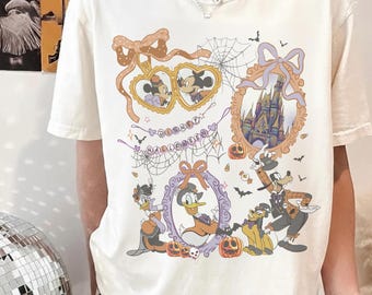 Puede incluir: Una camiseta de manga corta color crema con un estampado gráfico de personajes de Disney con disfraces de Halloween. El diseño incluye a Mickey y Minnie en marcos de corazón, un castillo, Goofy, Pluto y el Pato Donald, con el texto DISNEY HALLOWEEN.