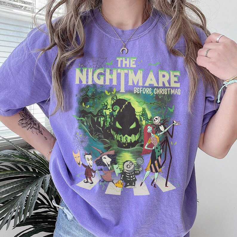 May include: A purple t-shirt featuring a graphic print of The Nightmare Before Christmas characters including Jack Skellington, Sally, and Oogie Boogie. The design includes the movie title in yellow text against a green and black background.