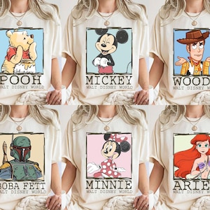 May include: A selection of cream-coloured t-shirts, each showcasing a different Disney character. The shirts feature framed images of Pooh, Mickey, Woody, Boba Fett, Minnie, and Ariel, with their names and "Walt Disney World" printed beneath each illustration.