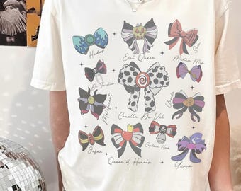 Puede incluir: Una camiseta de color crema con un estampado gráfico de varios lazos inspirados en villanos ficticios. Cada lazo está etiquetado con nombres que incluyen Hades, Evil Queen, Scar, Dr. Facilier, Cruella De Vil, Ursula, Maleficent, Jafar, Queen of Hearts, Captain Hook y Yzma.