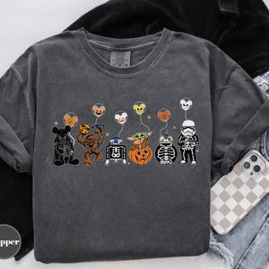 Puede incluir: Camiseta gris oscuro con personajes de dibujos animados disfrazados para Halloween. Los personajes incluyen Mickey Mouse, Chewbacca, R2-D2, Baby Yoda y un Stormtrooper, cada uno sosteniendo un globo. La palabra "Pepper" est&aacute; en la esquina inferior izquierda.
