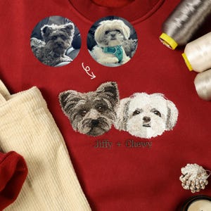 May include: Red sweatshirt with embroidered images of two dogs, a black and brown dog and a white dog. The text "Jiffy + Chewy" is embroidered below the dogs.